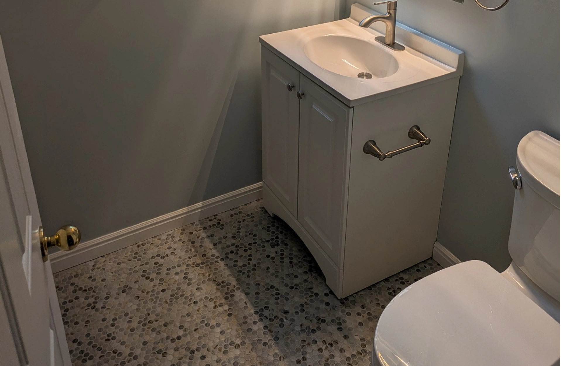 A full view of a small bathroom with gray walls, a window, a toilet, and a white vanity with a sink.